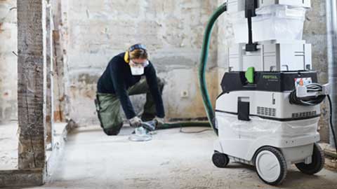 Un artisan ponce un sol en utilisant le système de ponçage des sols Festool avec aspiration.