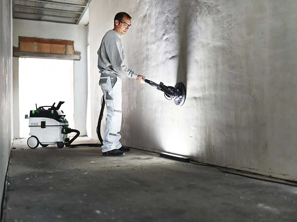 Een vakman verlicht een muur met behulp van het Strijklicht van de schilder en schuurt hem af