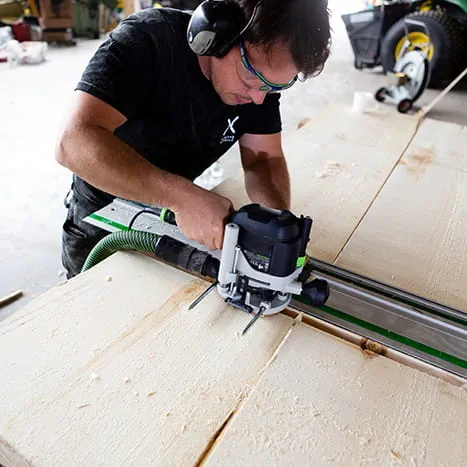 Un constructeur de saunas en train de travailler une surface avec une défonceuse de Festool.